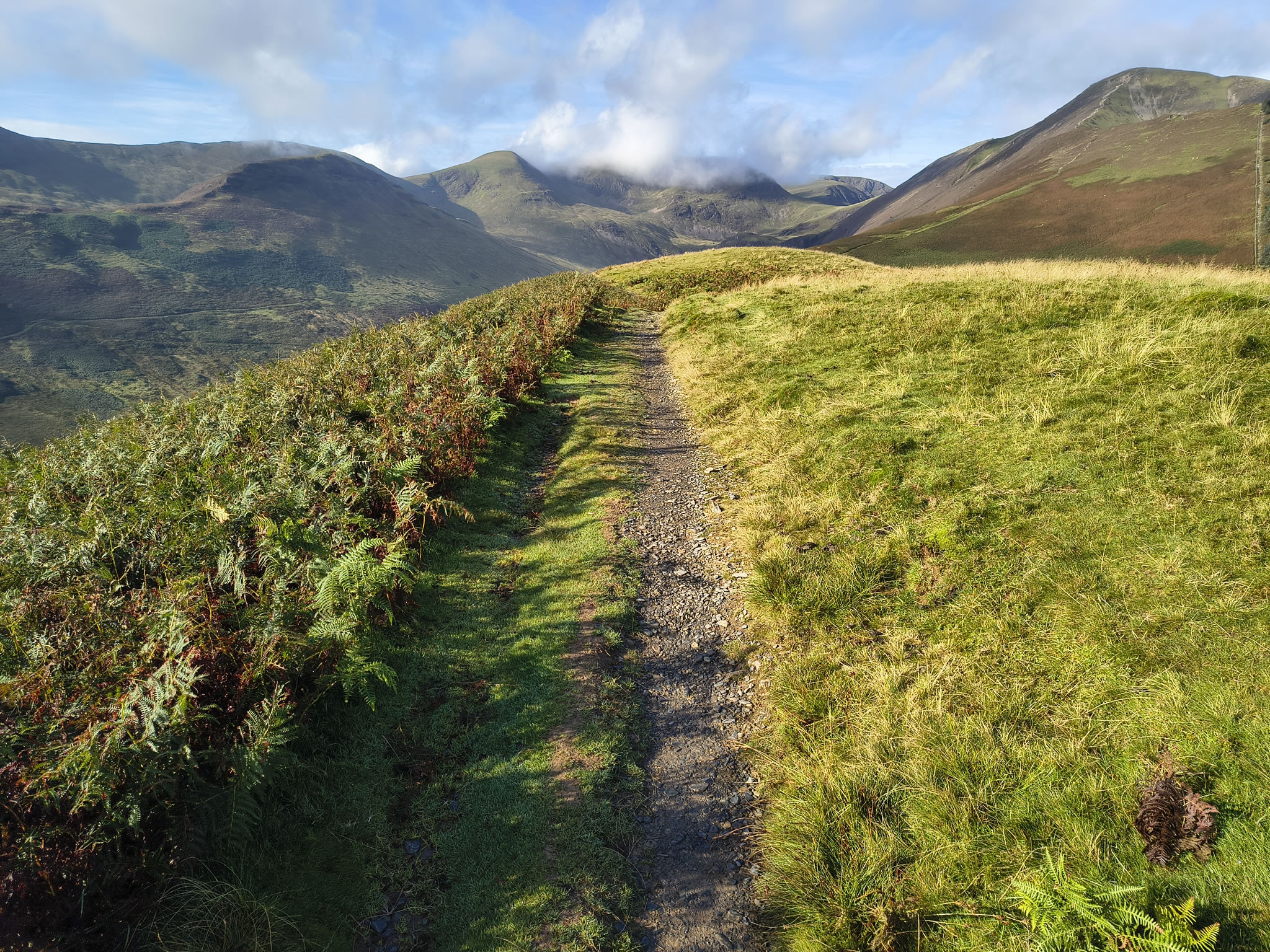 Path from Kinn, grass and bracken. Grisedale Pike to the right, clouds above Coledale Hause. Cloudy blue sky, Sep 09, 2025